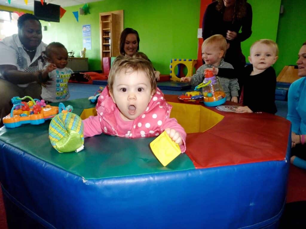 A group of parents participating in Child Fitness Classes with a baby in a play room.