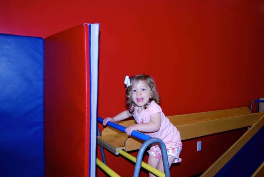 A child participating in Child Fitness Classes standing on a ladder in a play area.