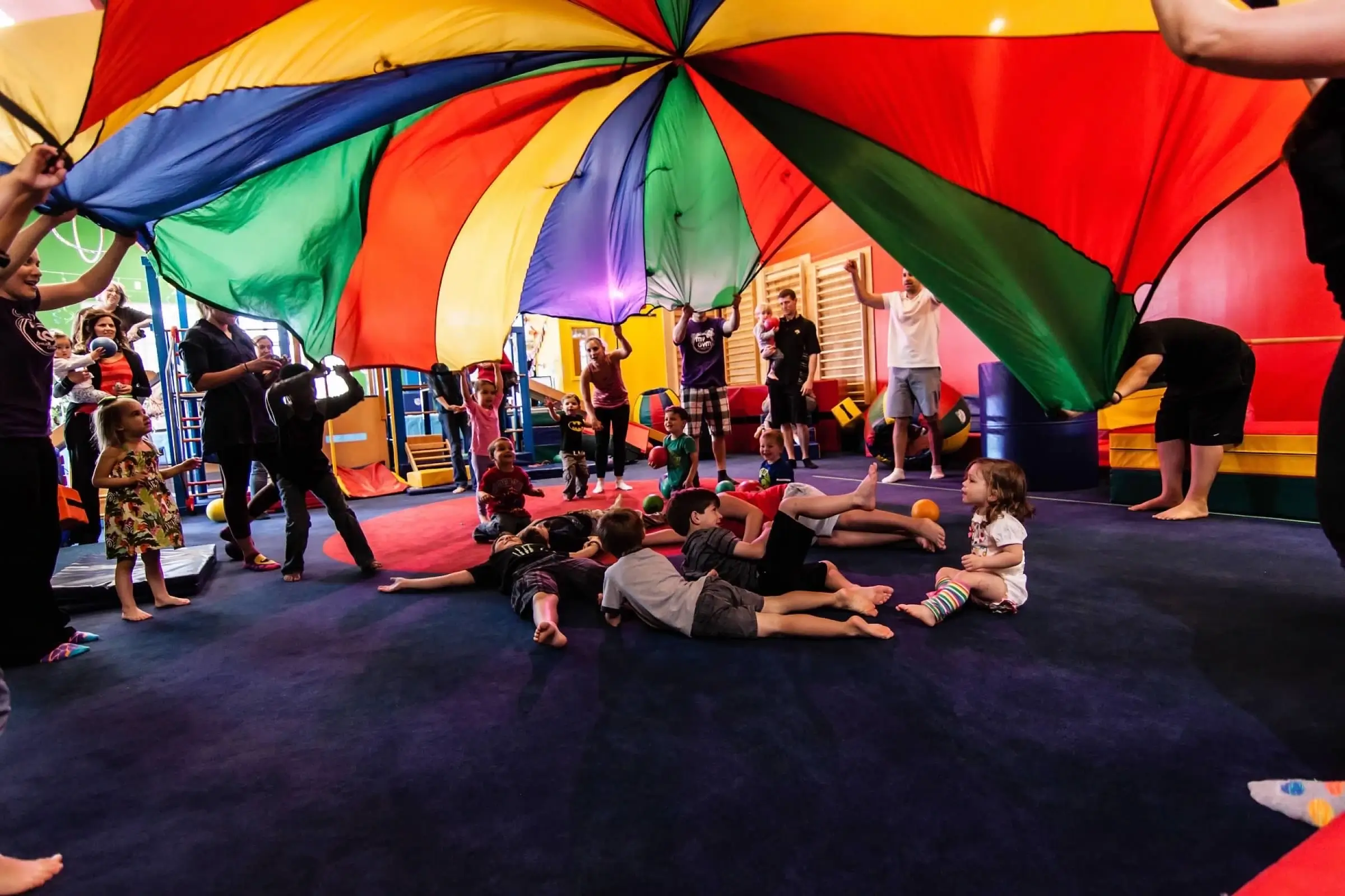 A group of kids engaged in fitness activities standing around a colorful parachute.