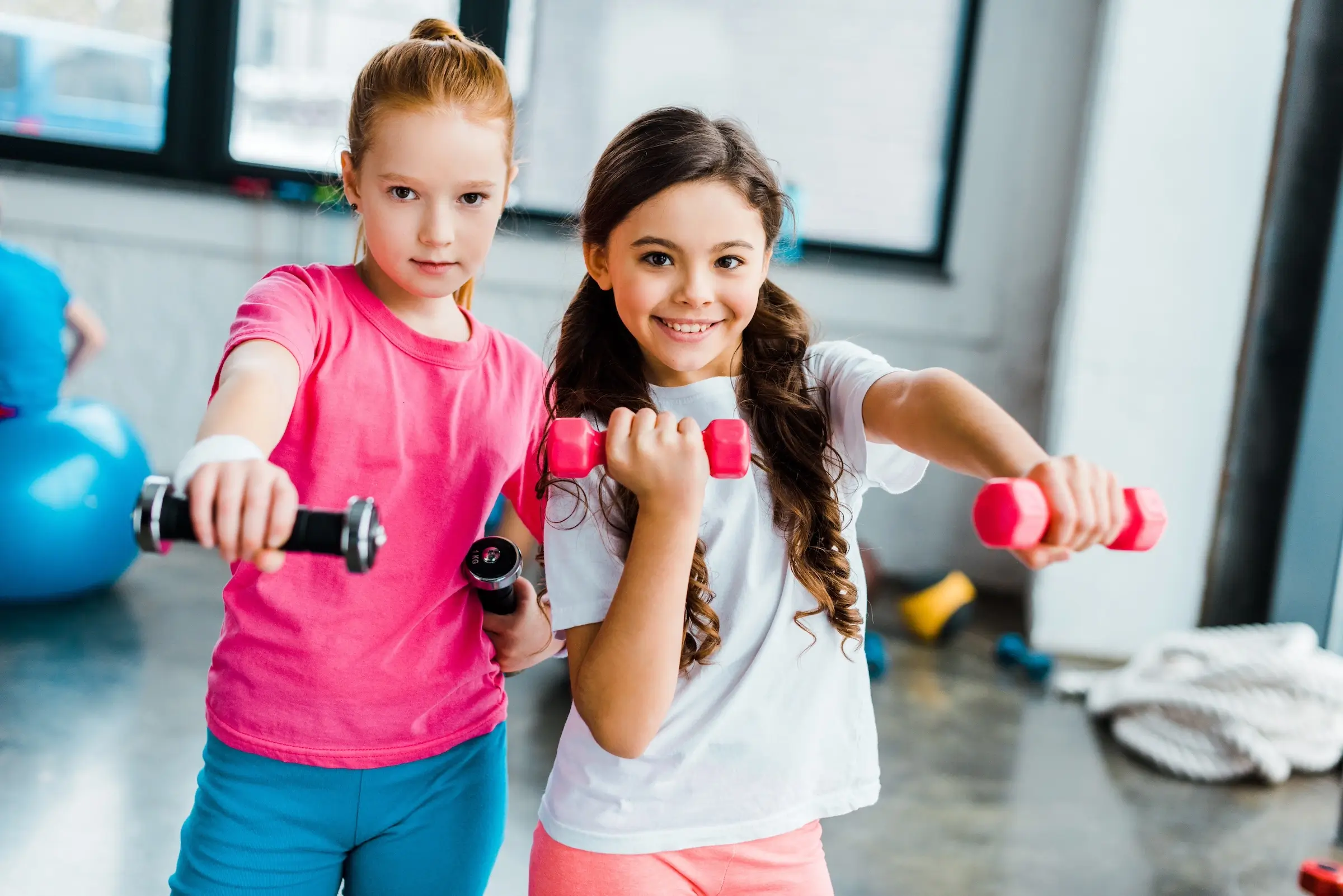 Two girls holding dumbbells in a gym.